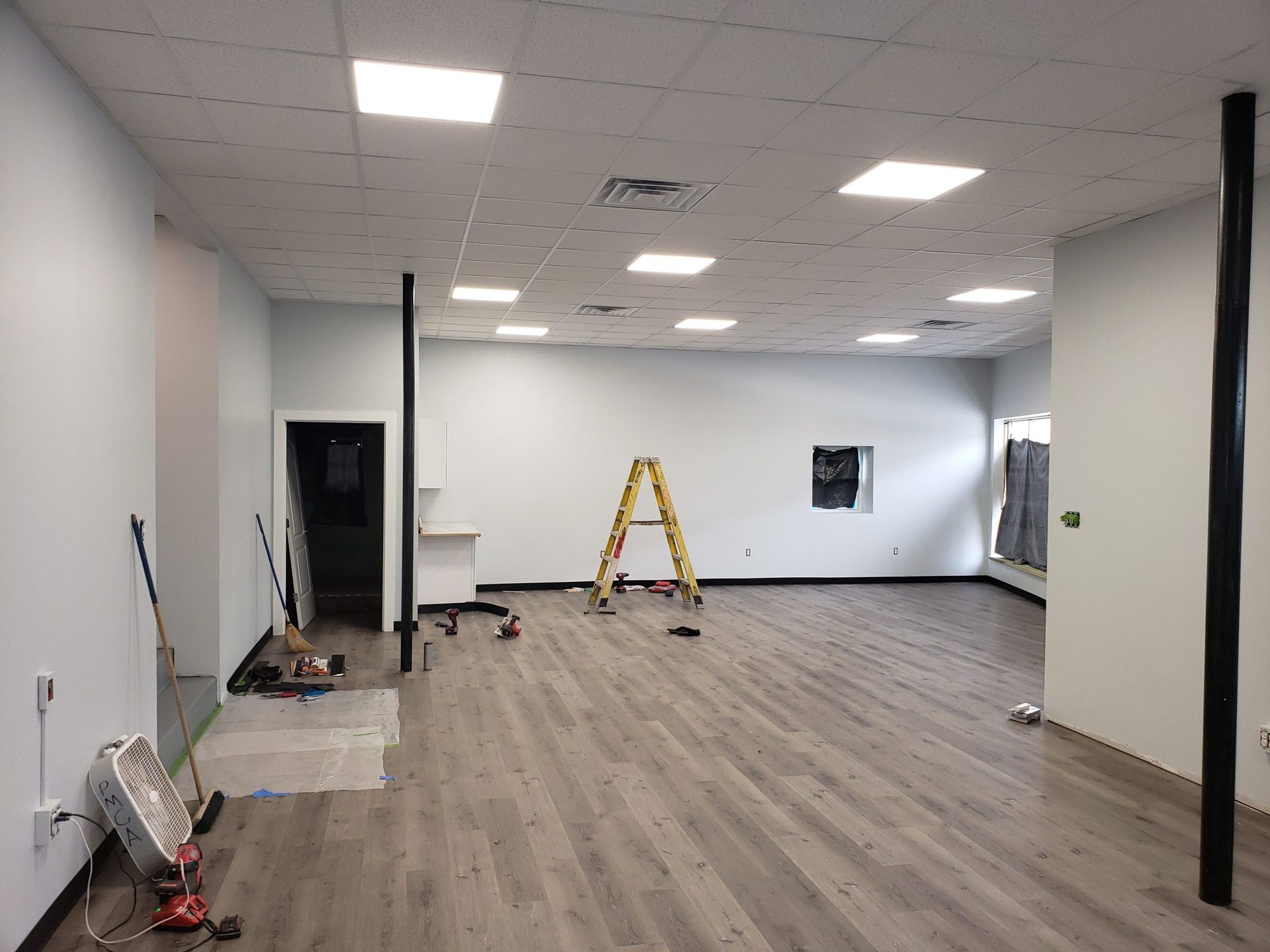 Interior of a room under construction with gray flooring, white walls, and black support beams.