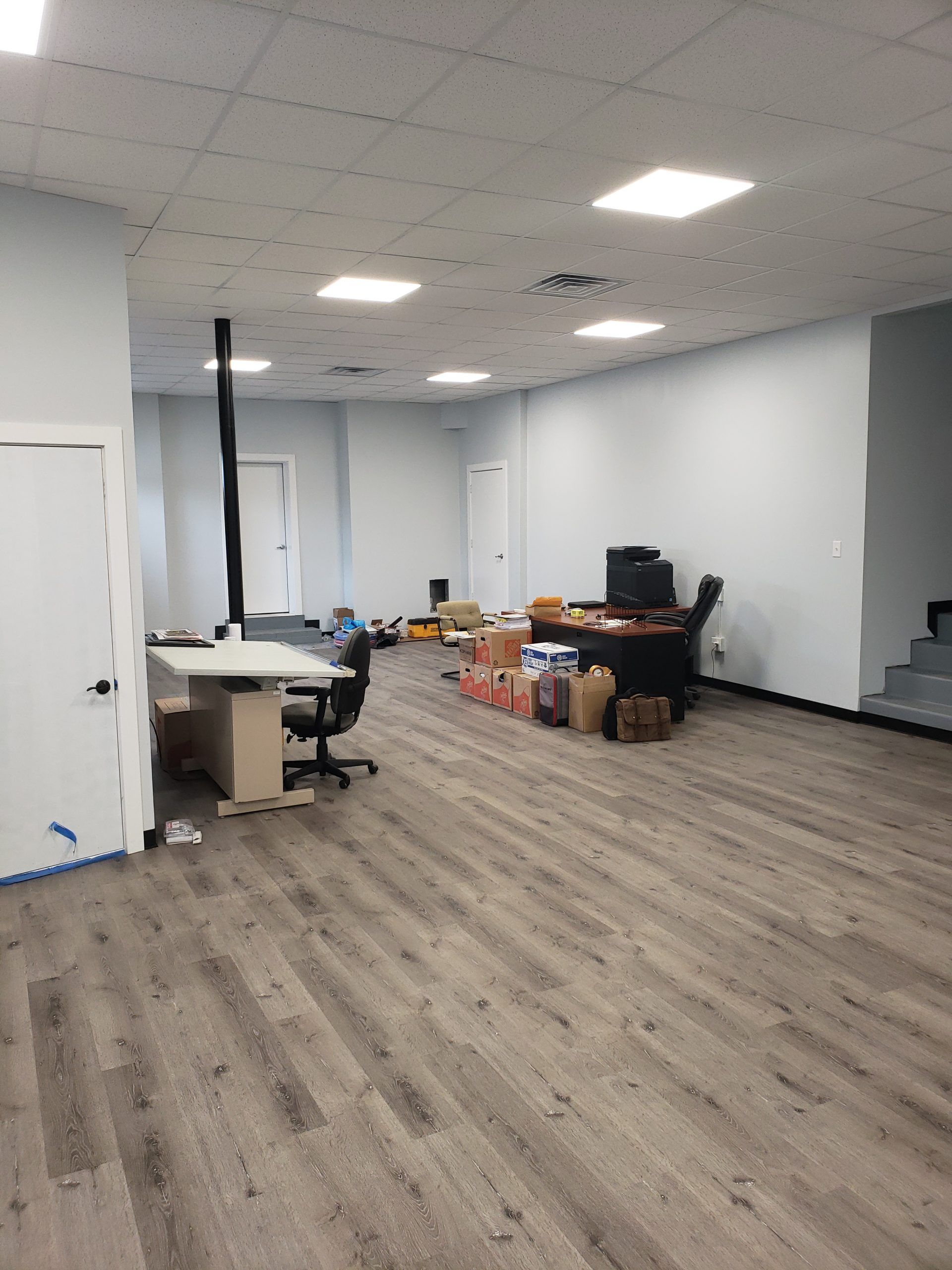 Empty office space with new gray wood-look flooring, white walls, and bright ceiling lights.
