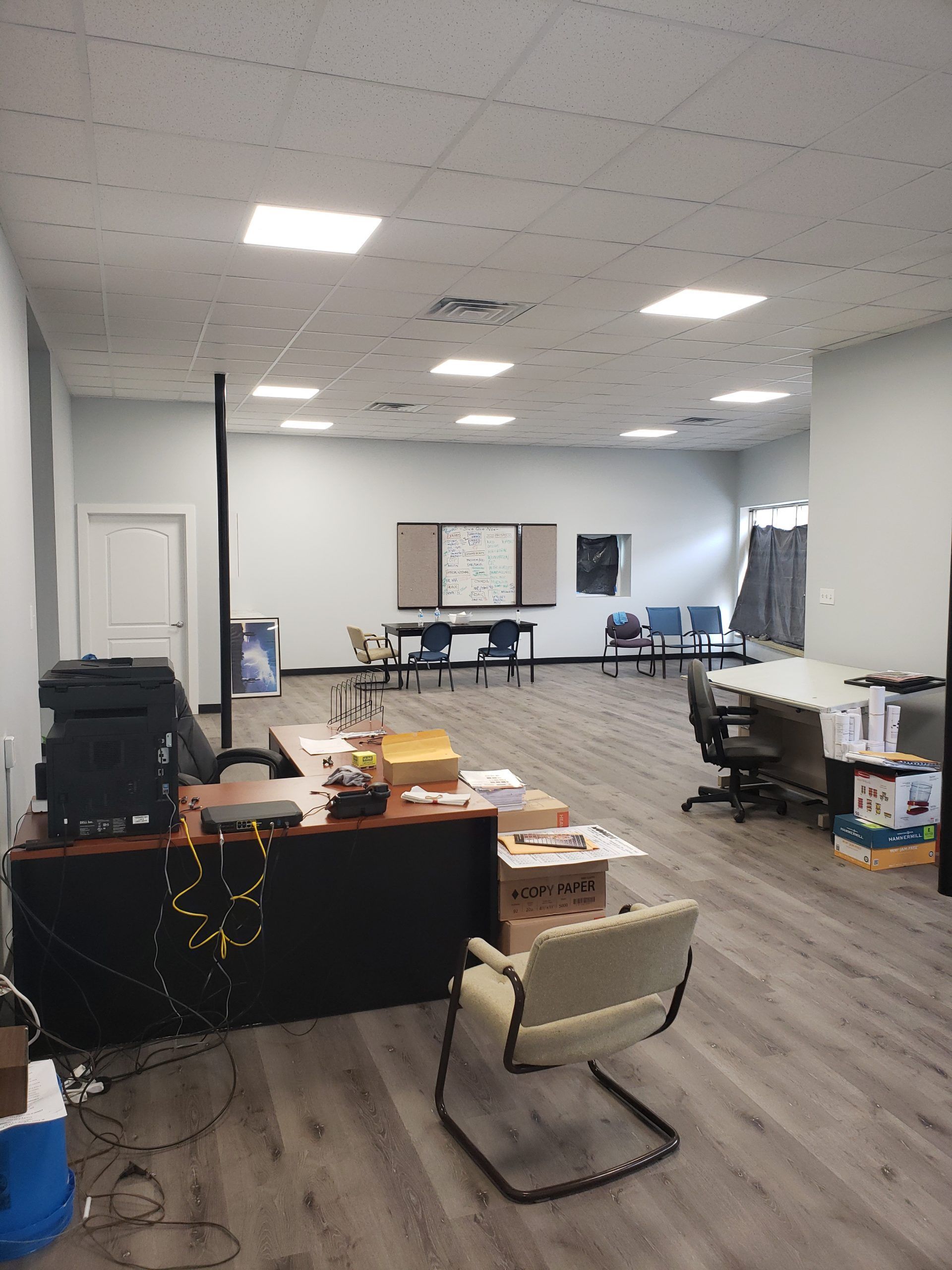 Office space with desk, chairs, tables, whiteboard, and grey flooring.