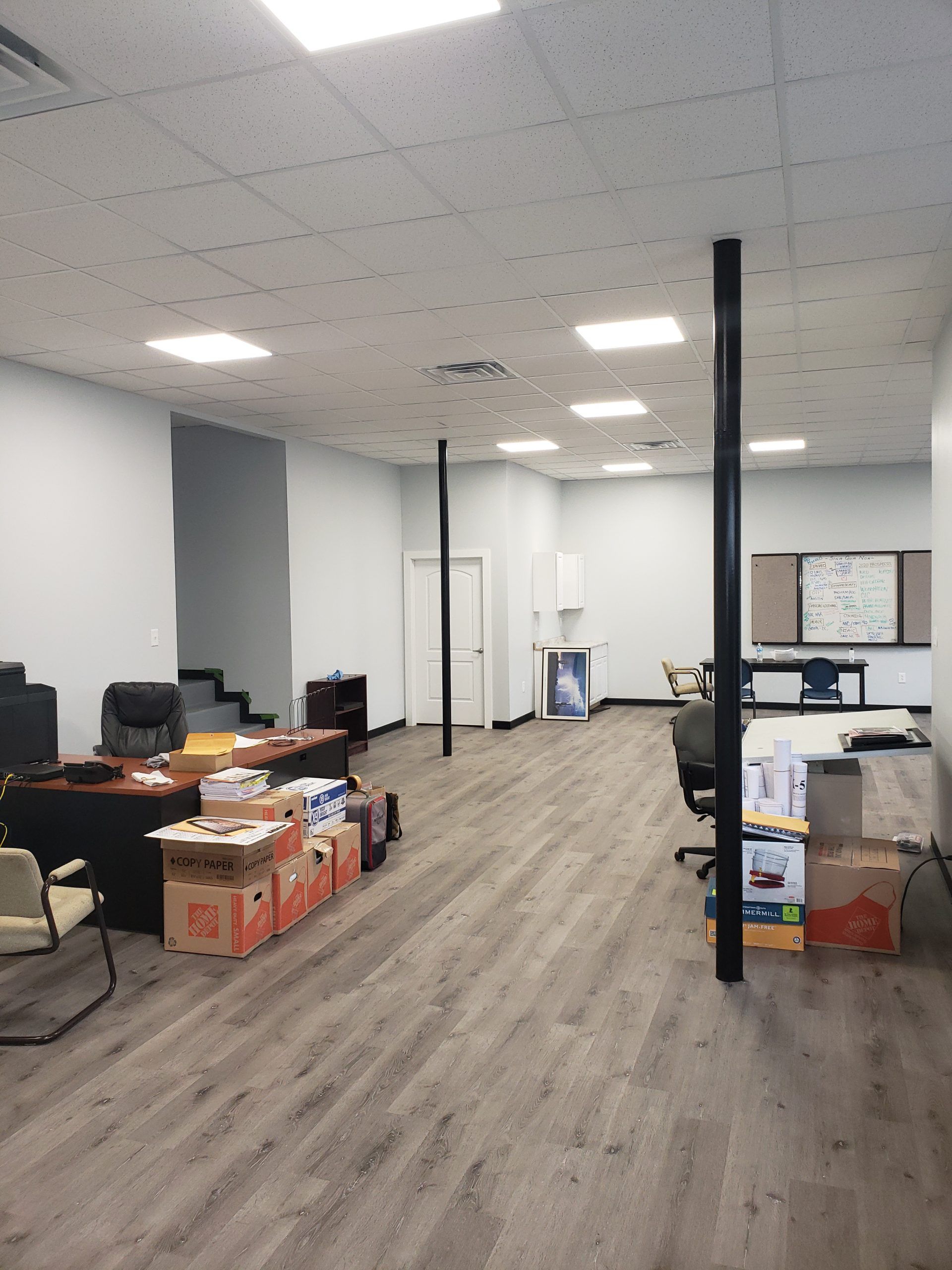 Empty office space with gray flooring, boxes, desks, and black support poles.