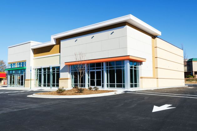 Modern commercial building with large windows and a paved parking lot on a sunny day.