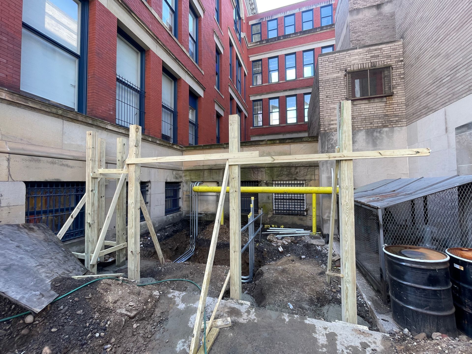 Wooden scaffolding erected in an alleyway between brick buildings, yellow gas pipes visible.