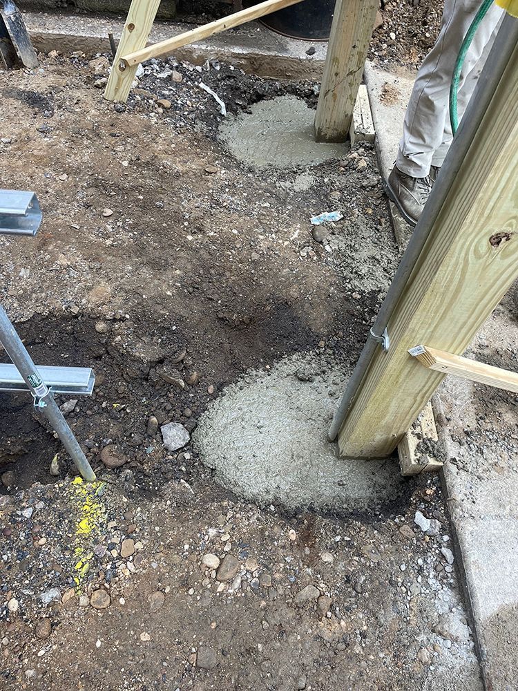 Construction site with wooden post set in wet cement, ground level view.