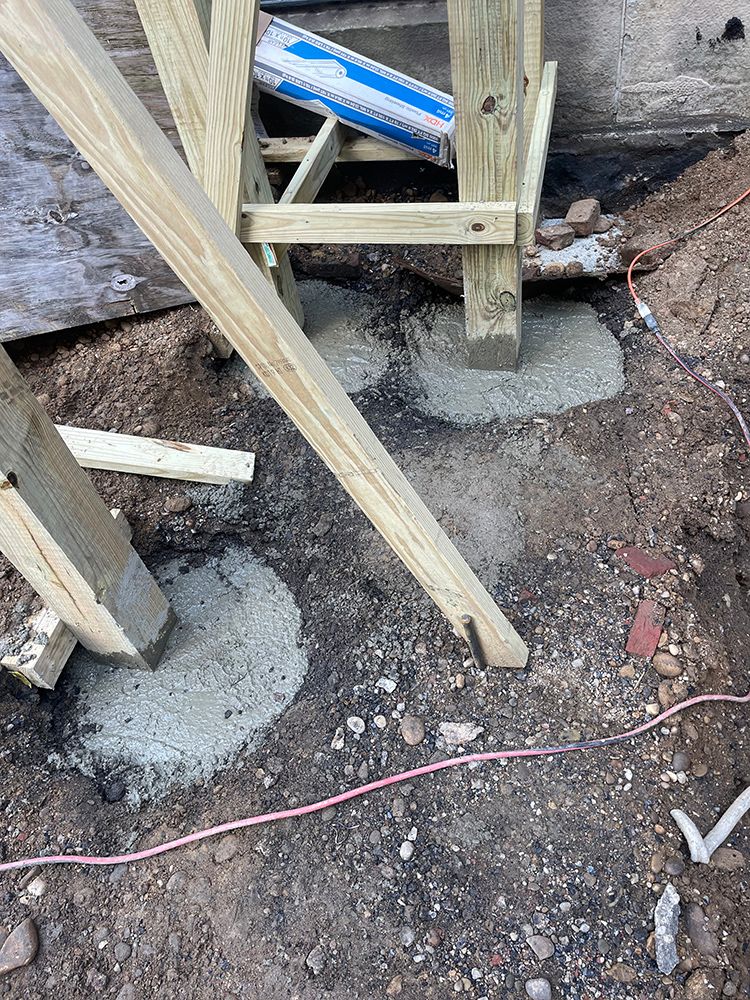 Wooden deck supports set in wet concrete footings on dirt ground.