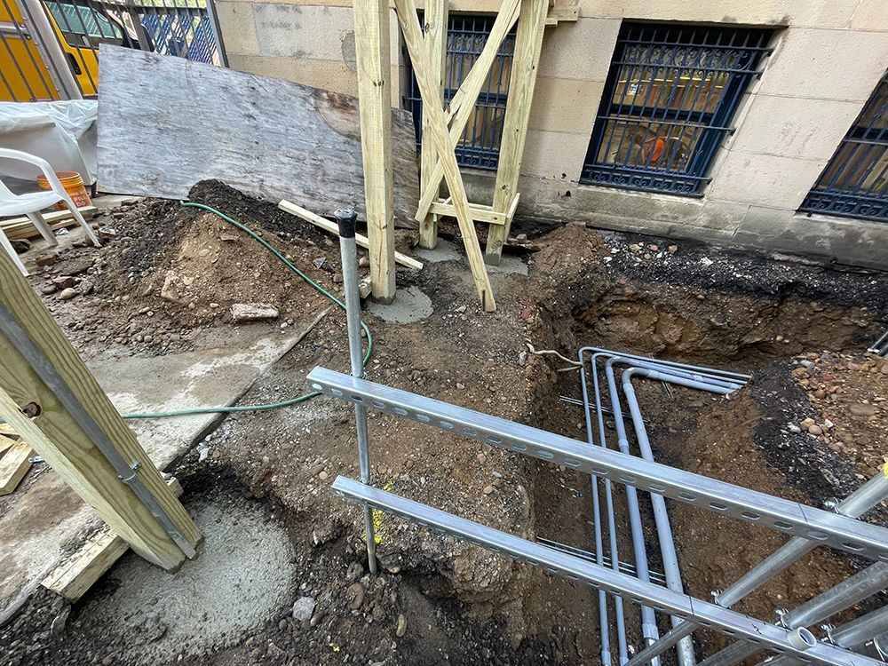 Construction site with exposed earth, concrete, and scaffolding next to a building.