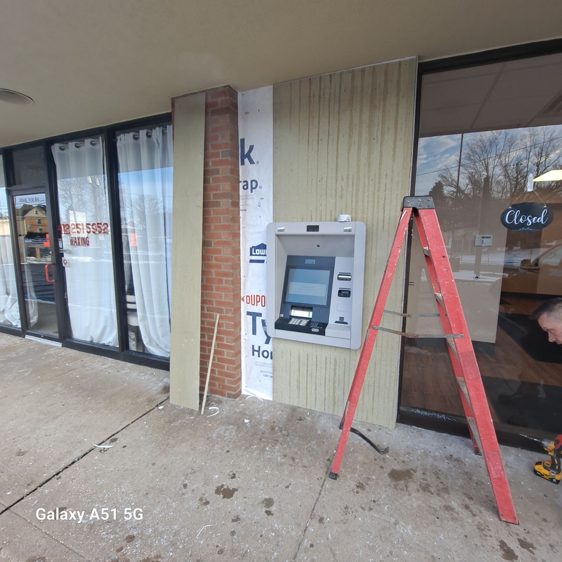 Exterior view of a building with an ATM. A person works on the wall near a ladder. 