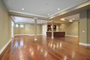 Spacious, empty room with hardwood floors, recessed lighting, and support columns; neutral walls.
