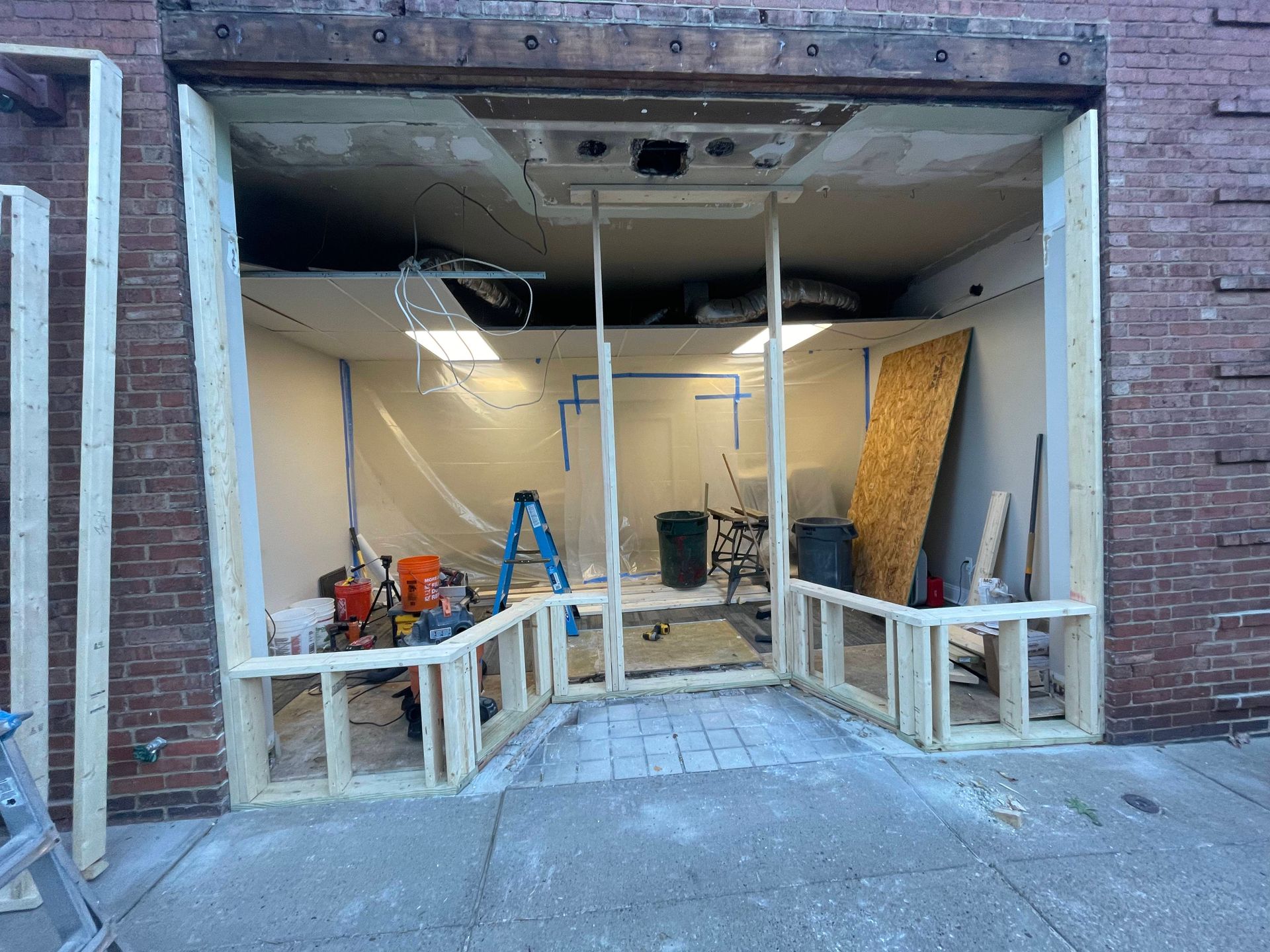Construction site, storefront entrance framed with wood, interior exposed, tools and debris visible.