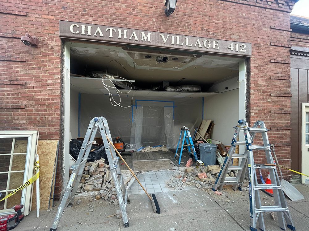 Exterior of Chatham Village building under construction; entrance damaged with debris and ladders.