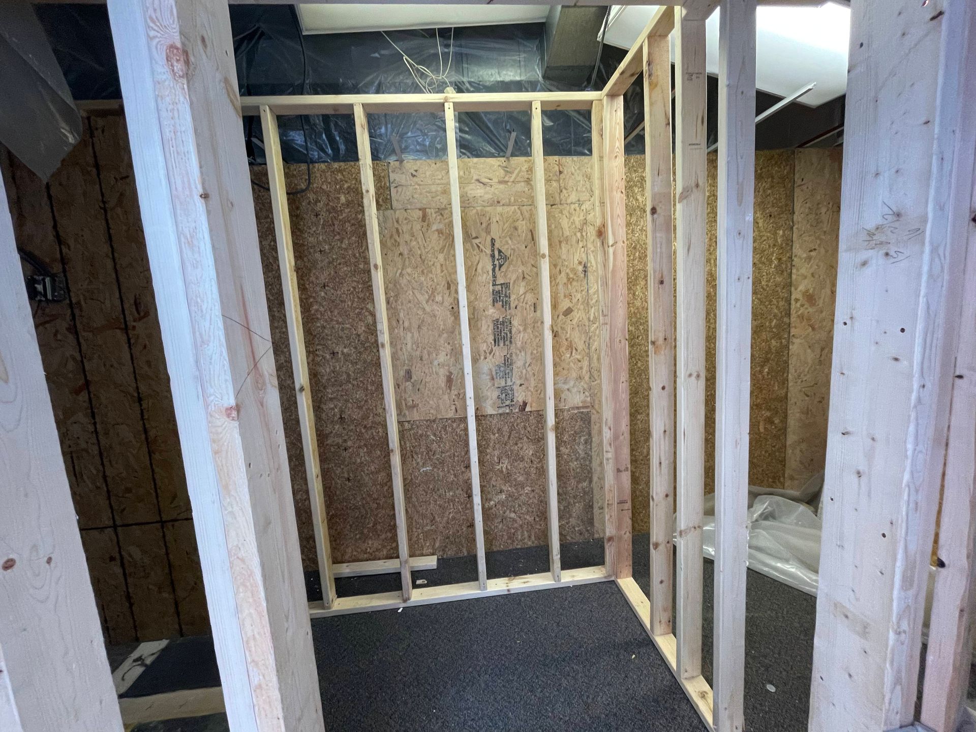 Interior view of a framed room under construction with exposed wooden studs and a black floor.