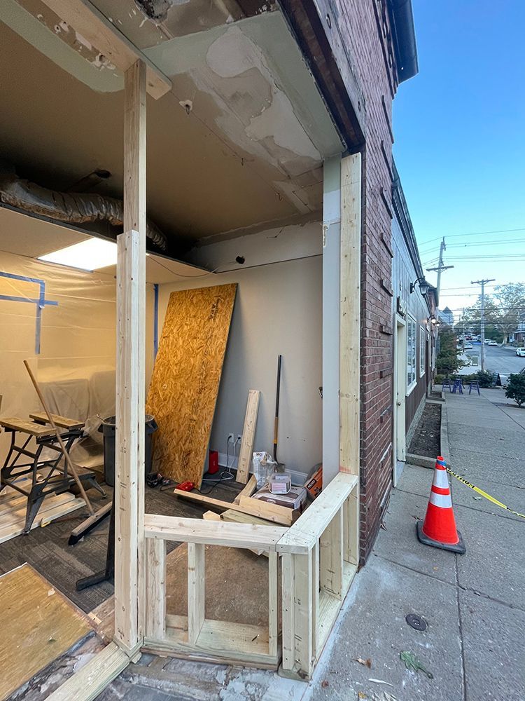 Construction site: doorway framed with wood on brick building exterior, orange cone on sidewalk.