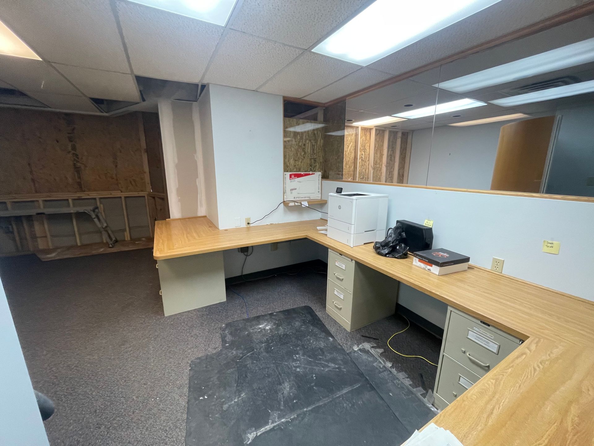 An office space with a U-shaped desk, a printer, and exposed wall construction.