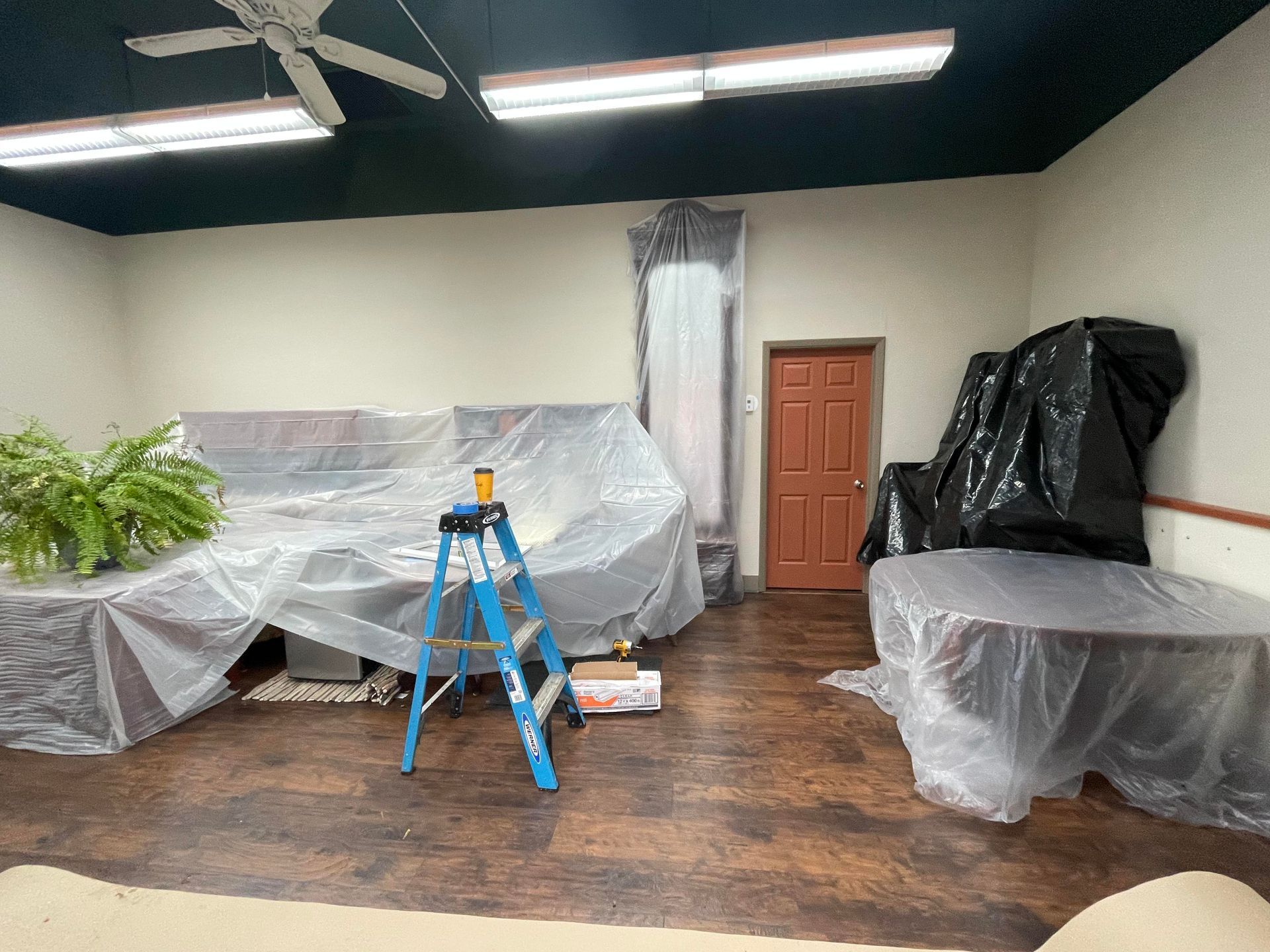 Interior room with furniture covered in plastic sheeting. A ladder stands nearby.