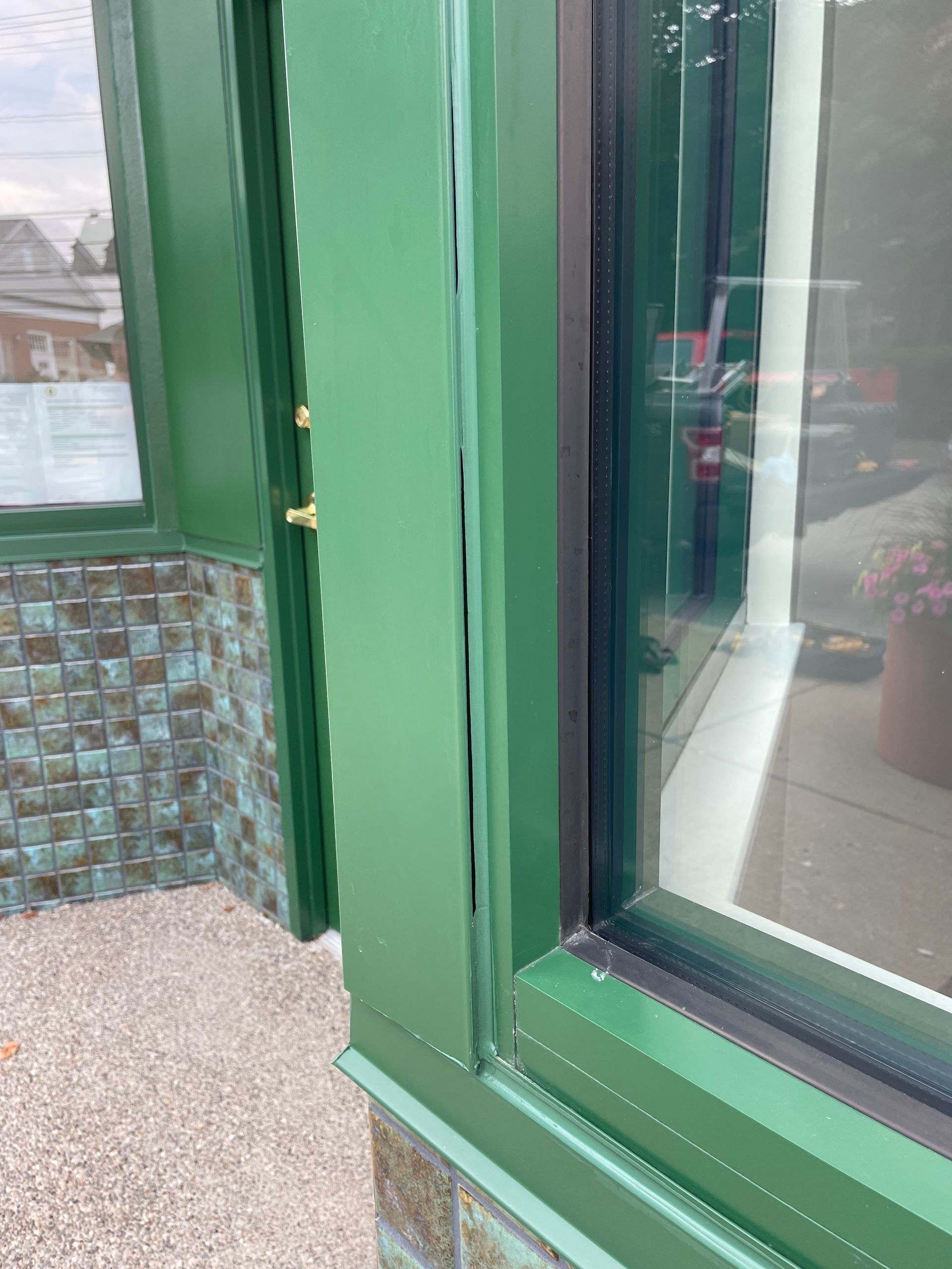 Green door frame with a vertical gap, next to a window, and tiled entry.