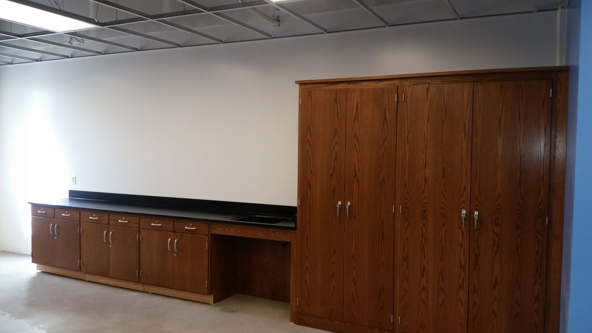 Wooden cabinets and counter against a white wall in a room with a drop ceiling.