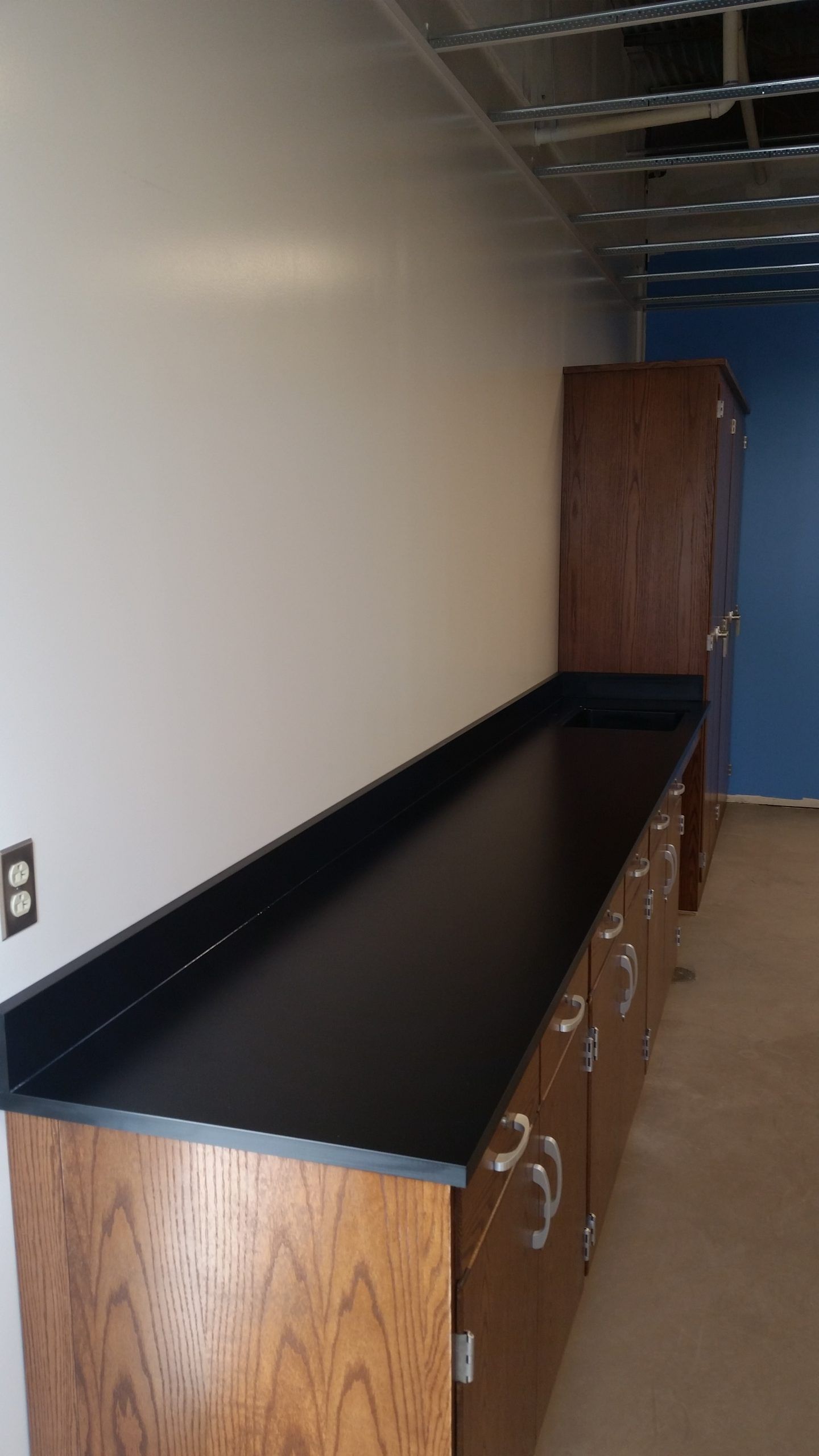 Long, black countertop with wood cabinets along white wall, brown cabinet in corner, blue door.