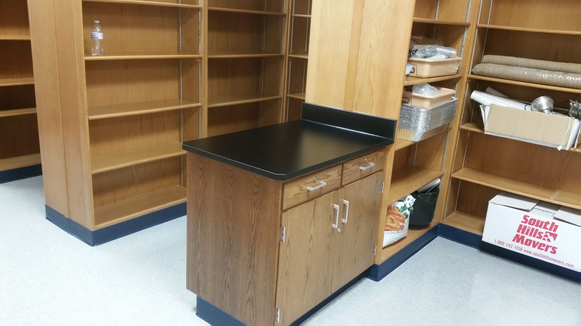 Wooden shelves and cabinet in a room. Cabinet has black countertop.
