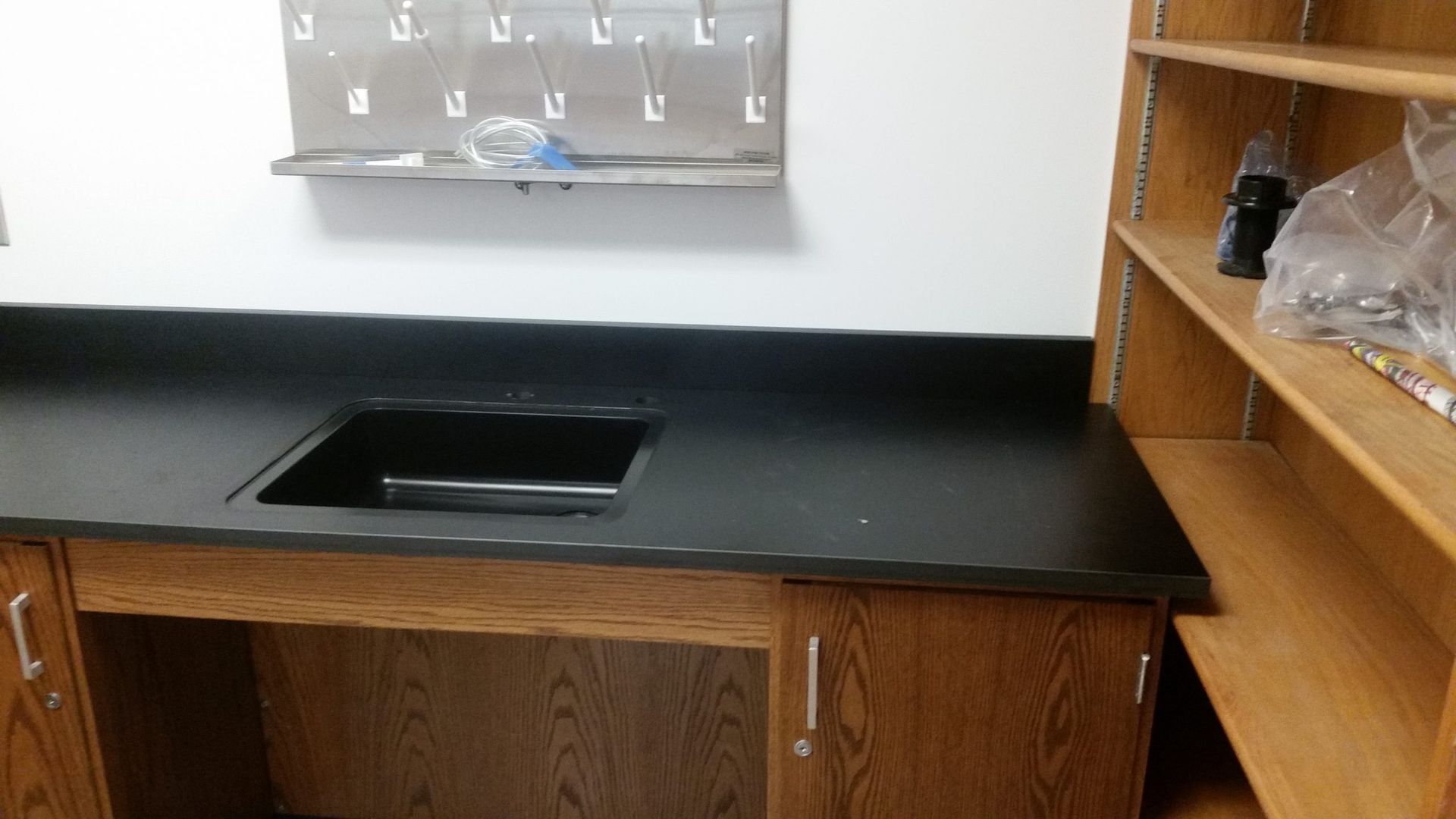Laboratory counter with sink, cabinets, shelves, and a rack hanging on the wall.