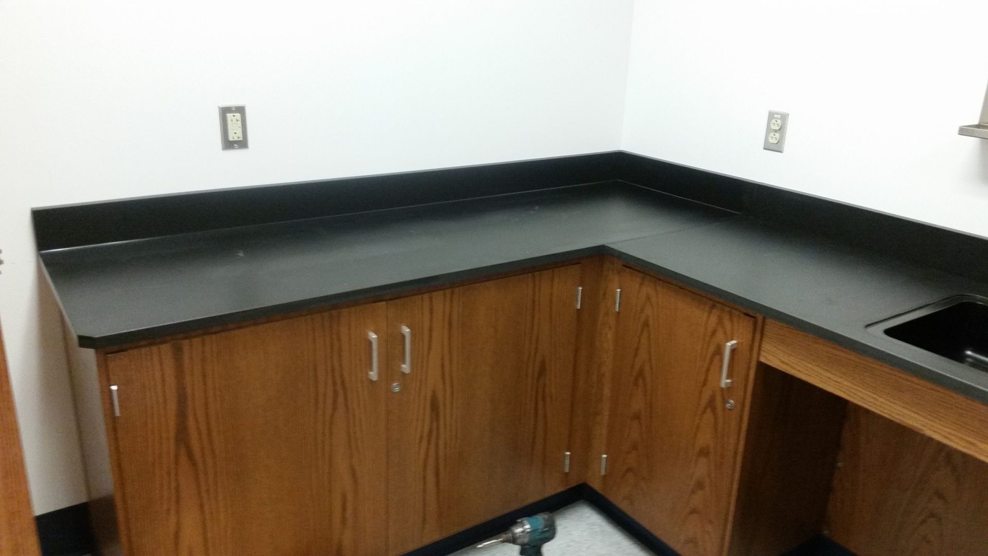 Corner cabinetry with a dark countertop and wooden cabinet doors. A sink is in the corner.