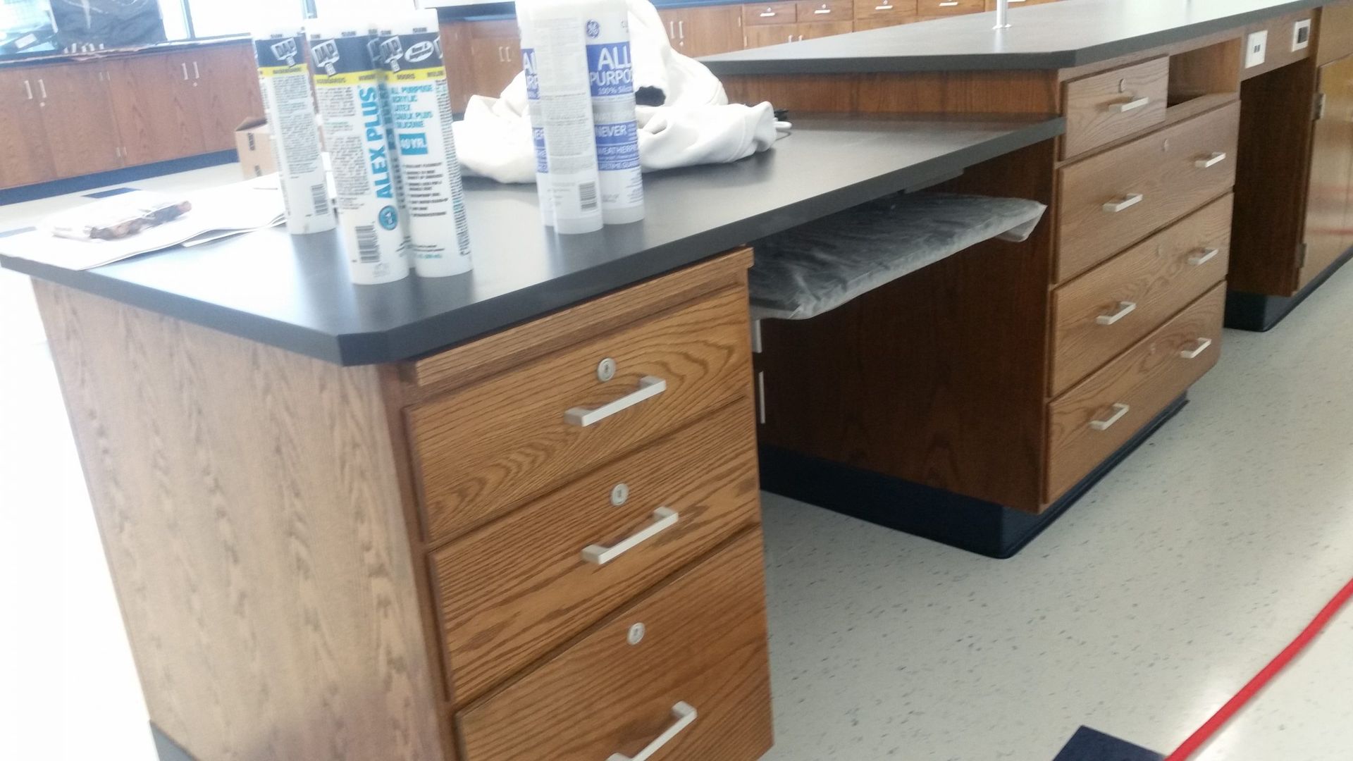 Wooden science lab desks with black countertops and drawers, with supplies on the surface.