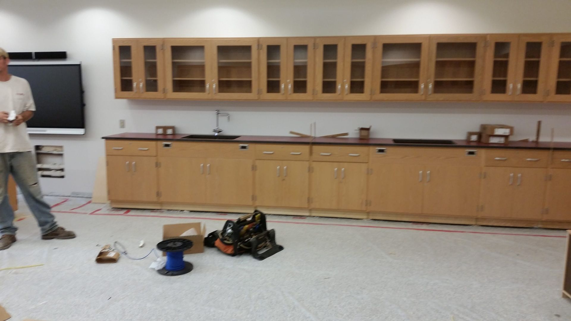 A person stands in a room with cabinets and lab equipment. Wires are on the floor.