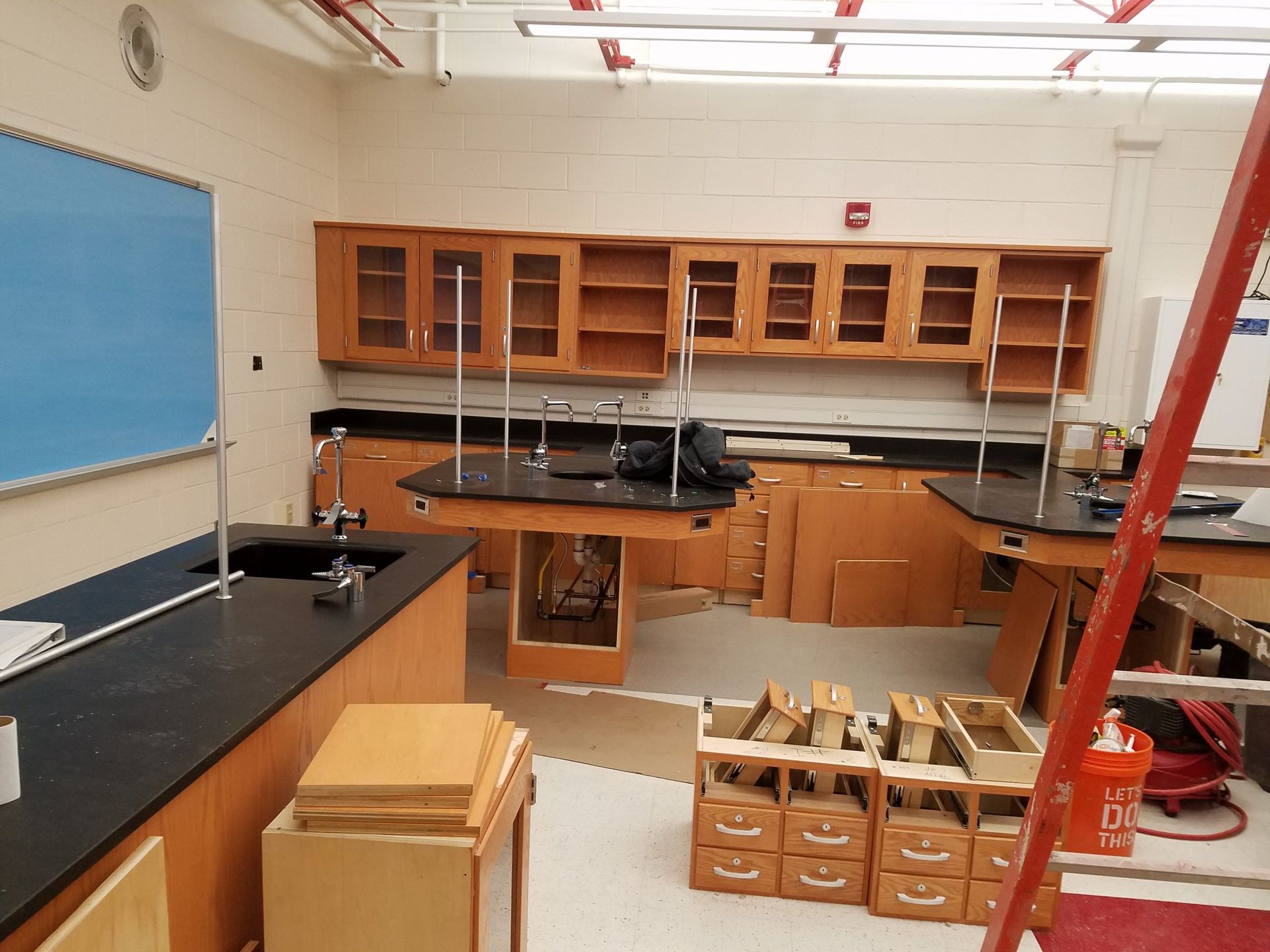 A science classroom under construction. Wooden cabinets, black countertops, lab tables, and a blue chalkboard.