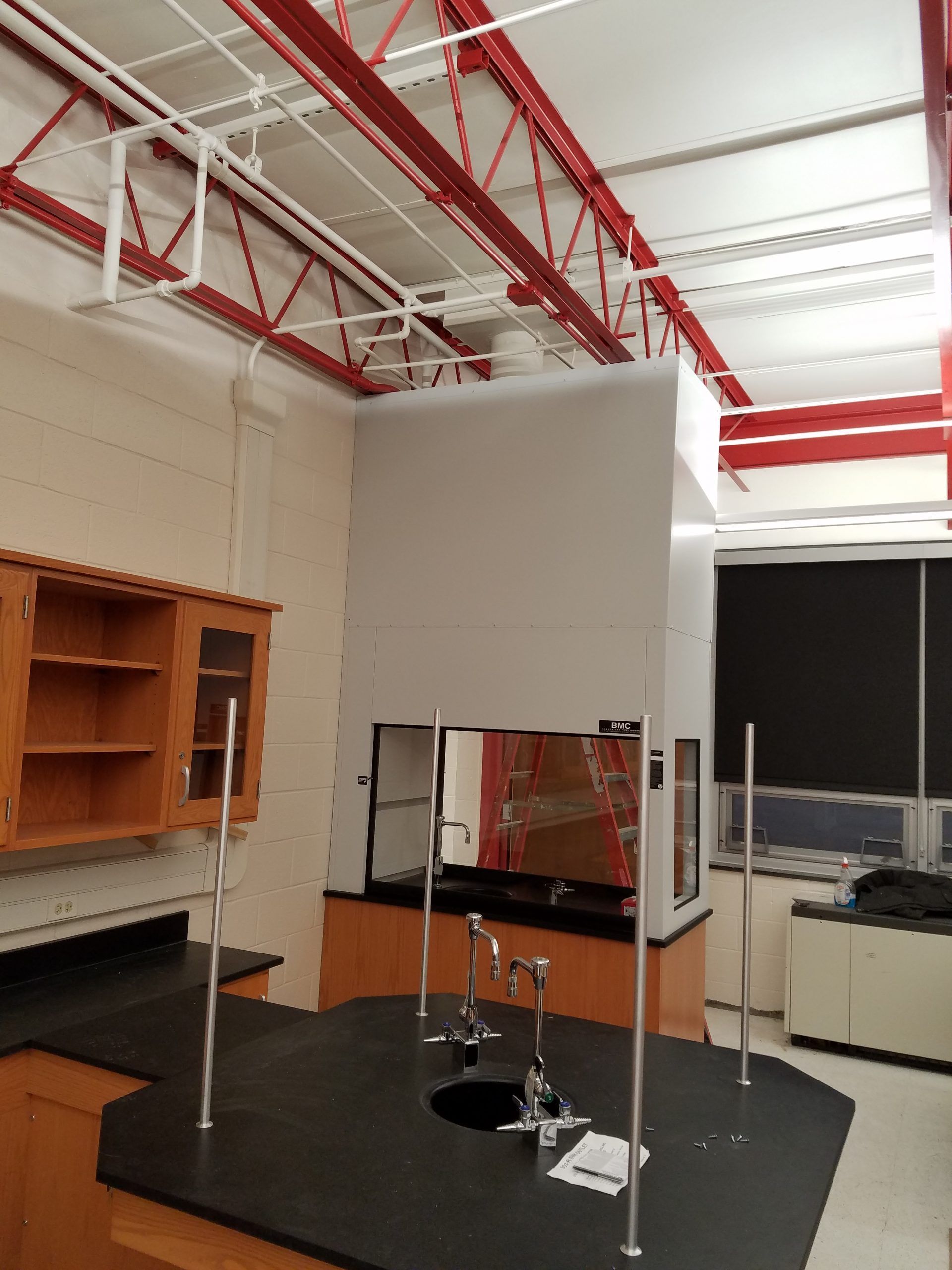 A lab with a fume hood and wooden cabinets. Red ceiling beams. Black countertops with lab faucets.