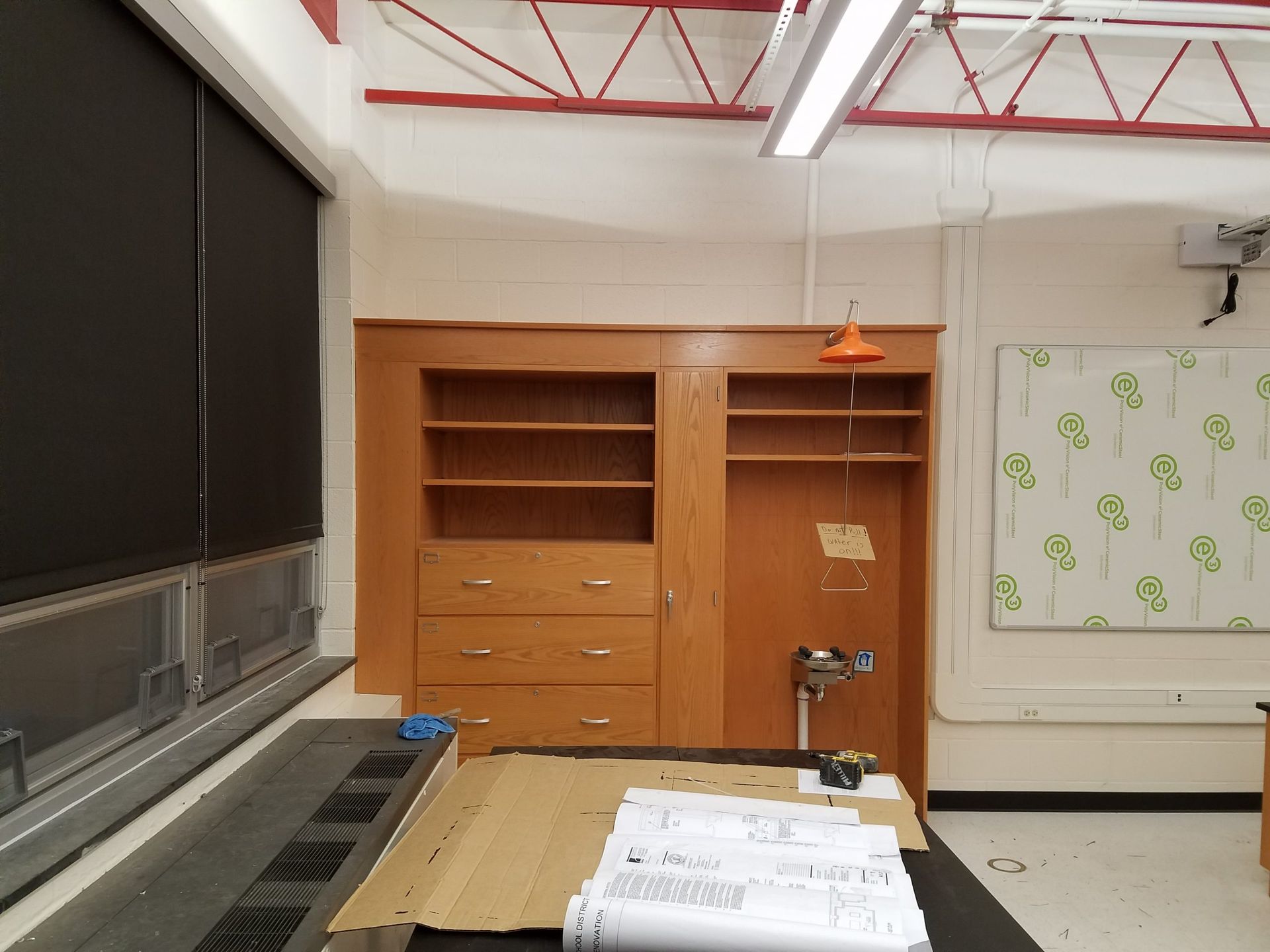 Wooden cabinet with shelves and drawers in a classroom; drawing materials on a desk.