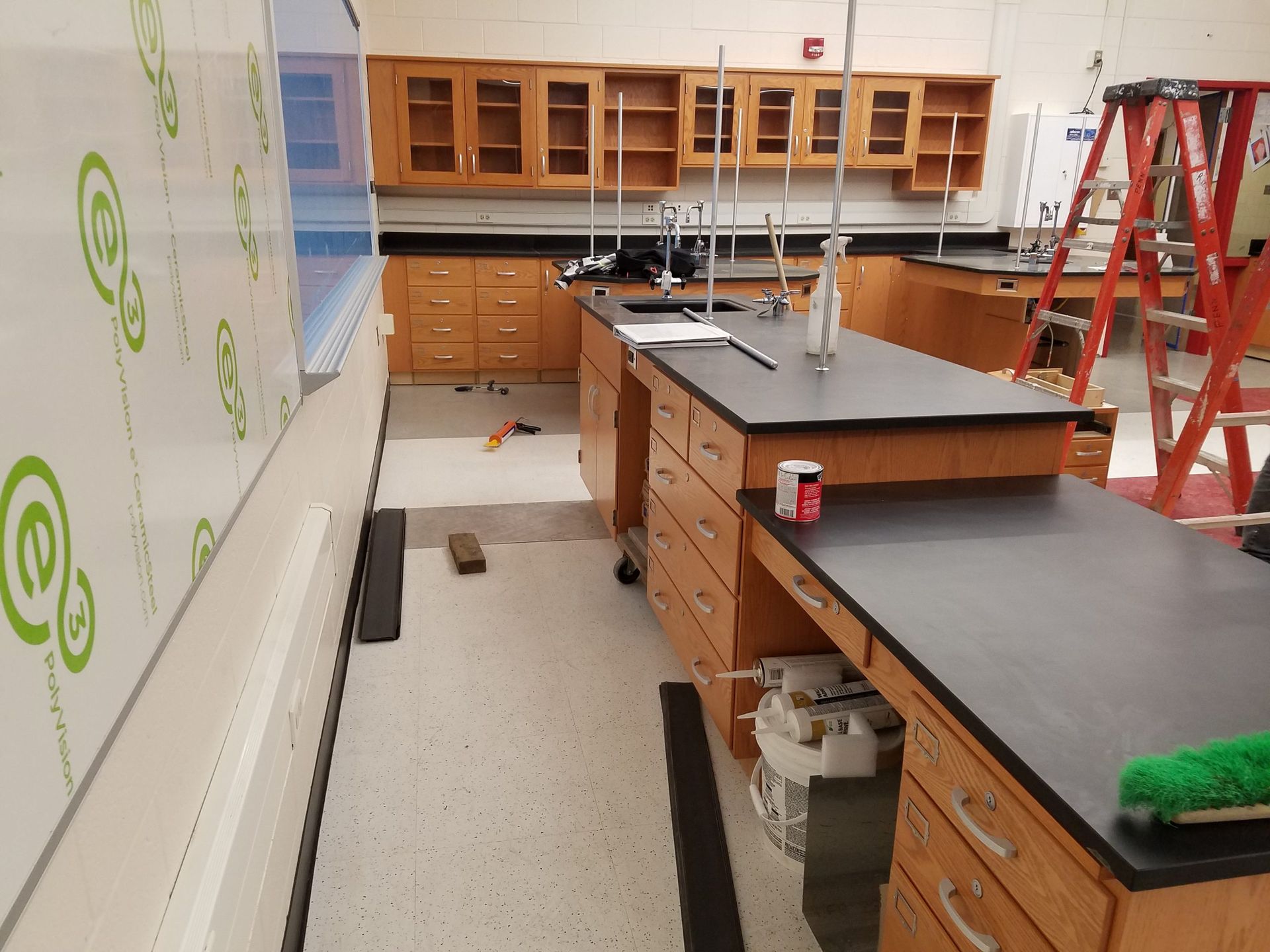Empty science classroom with lab tables, cabinets, and a ladder against the wall.
