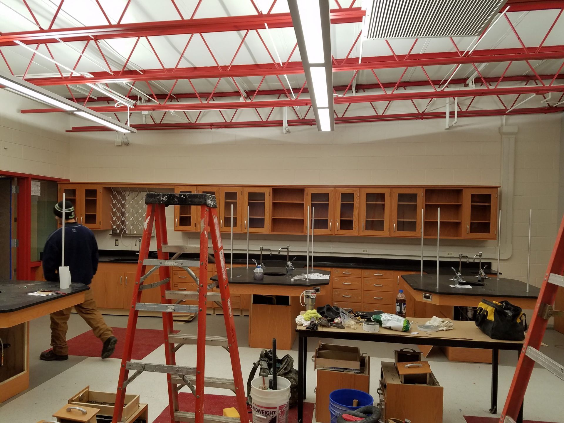 Interior of a lab being renovated with cabinets, lab tables, ladders, and a person working. Red ceiling beams.