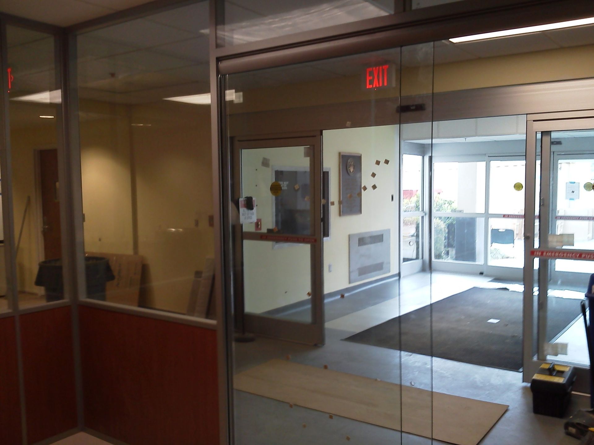 Glass doors leading to an interior with a desk and an exit sign.