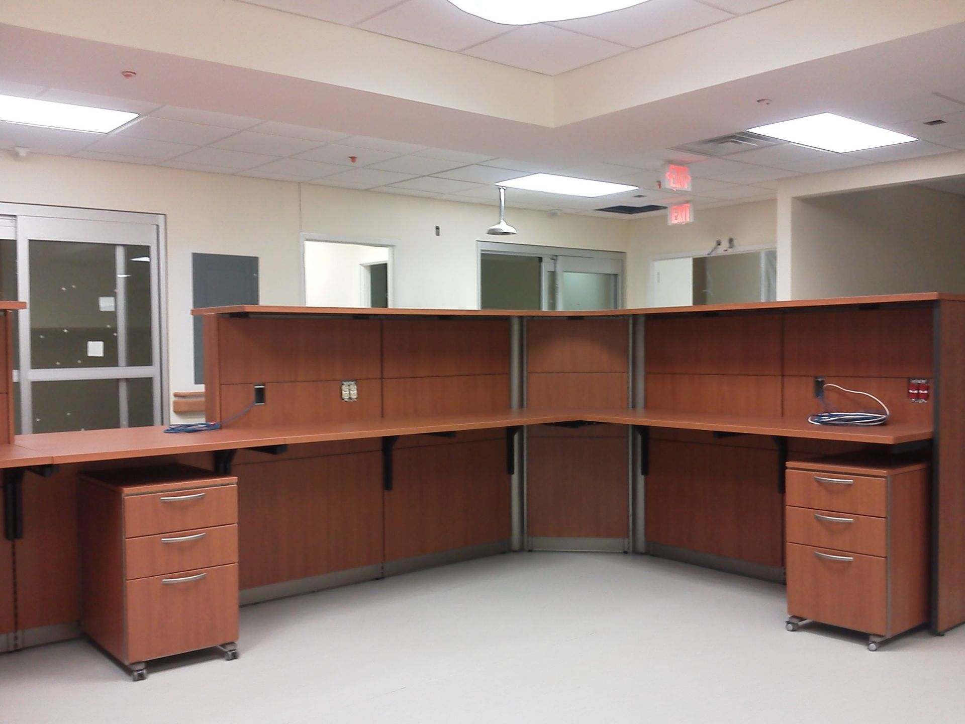Reception desk in a medical office, brown cabinets, light-colored walls and floor, automatic doors in the background.