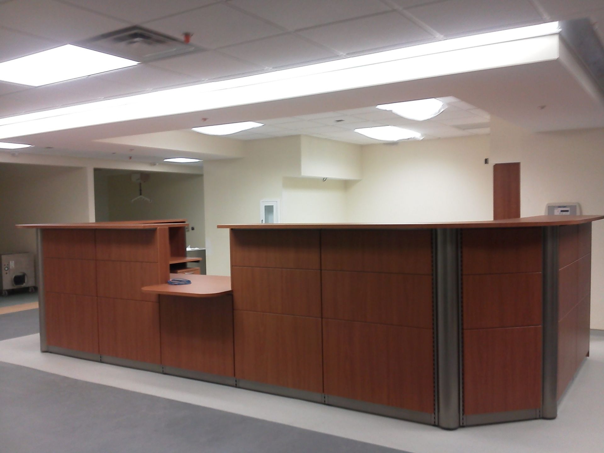 A modern reception desk in a brightly lit room. Brown wood, metal trim, and beige walls.