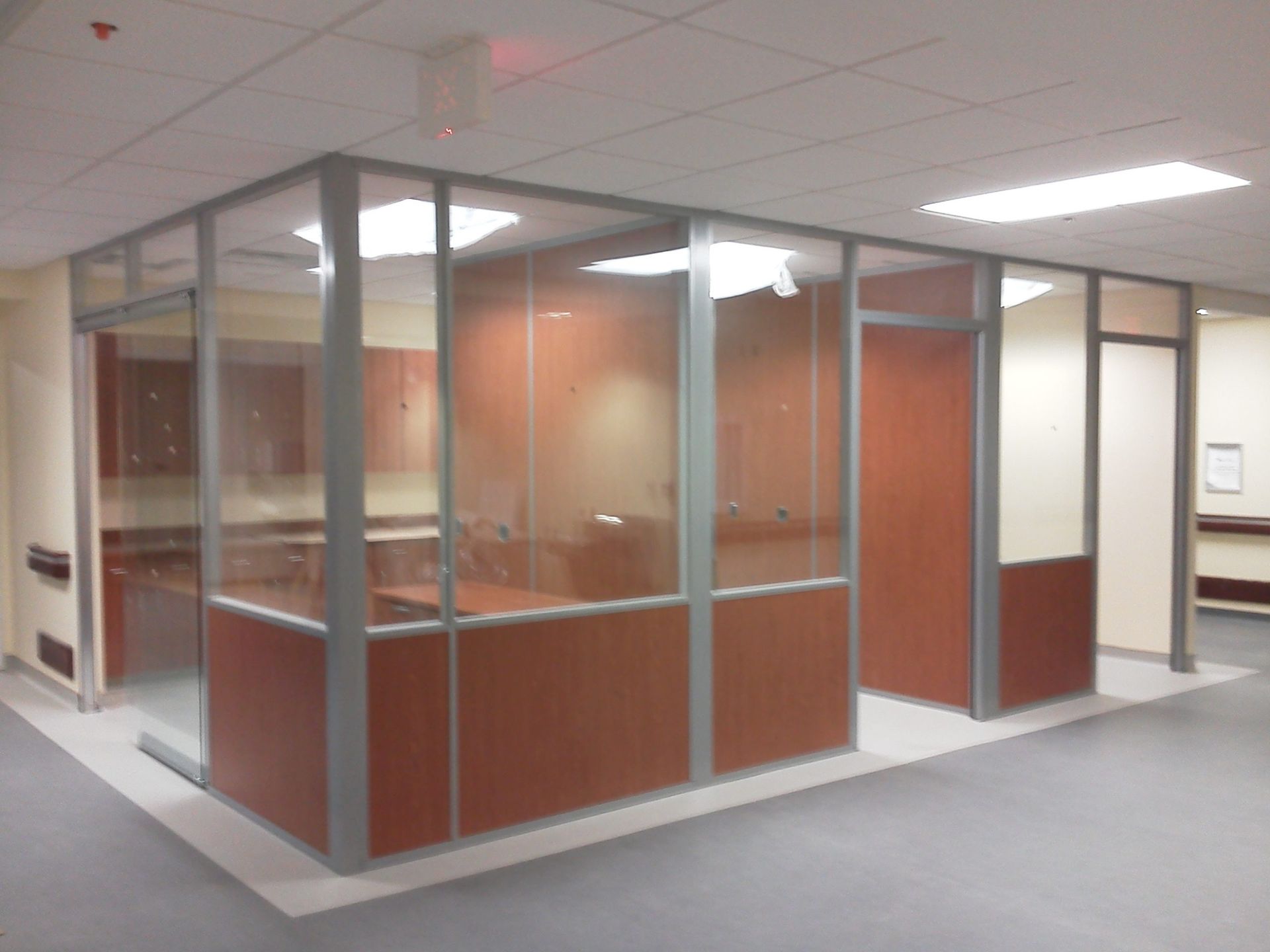 Office cubicles with glass and wood panels, in a modern hallway.