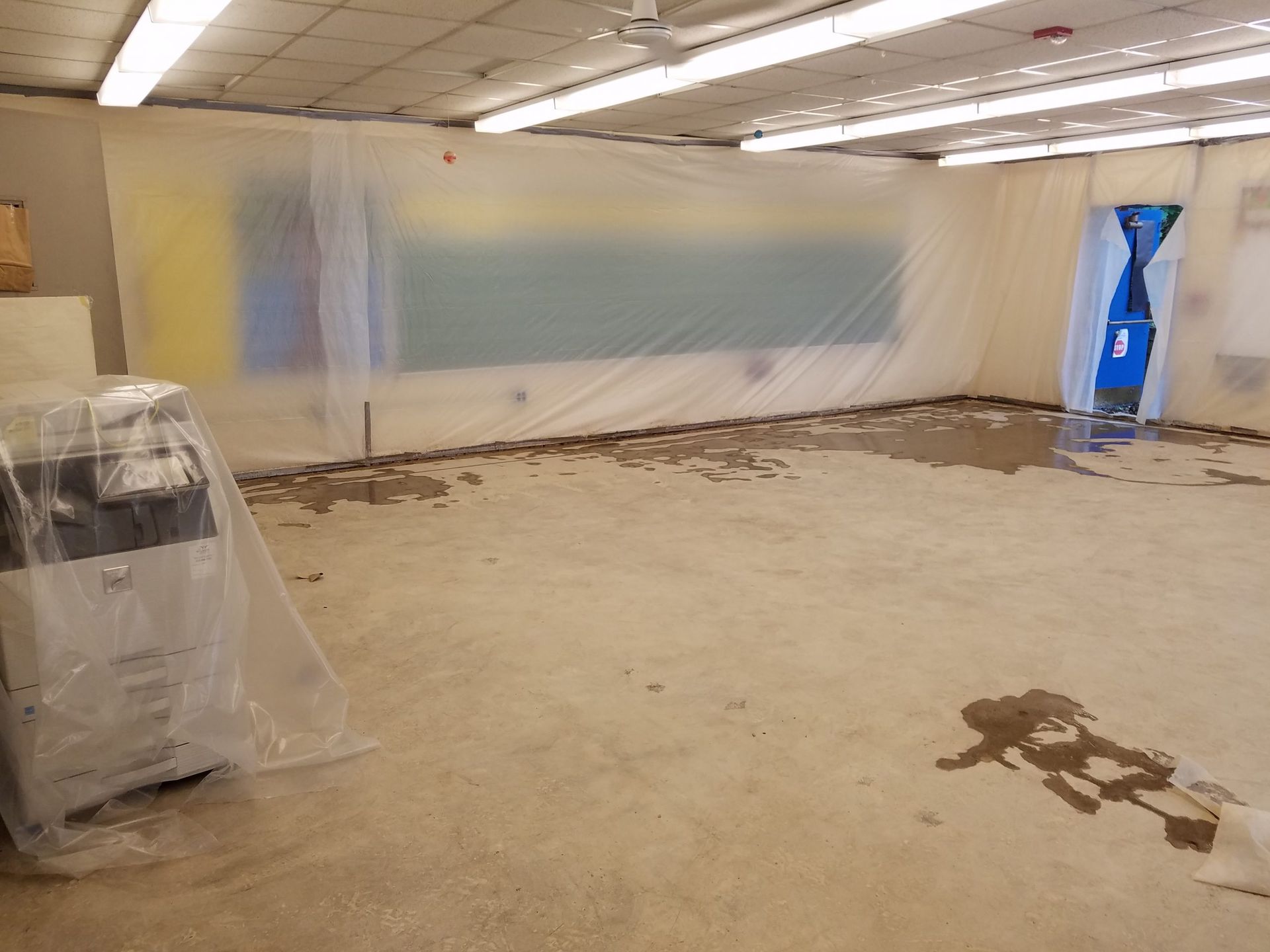 Room under construction, with plastic sheeting covering walls. Concrete floor has water damage.