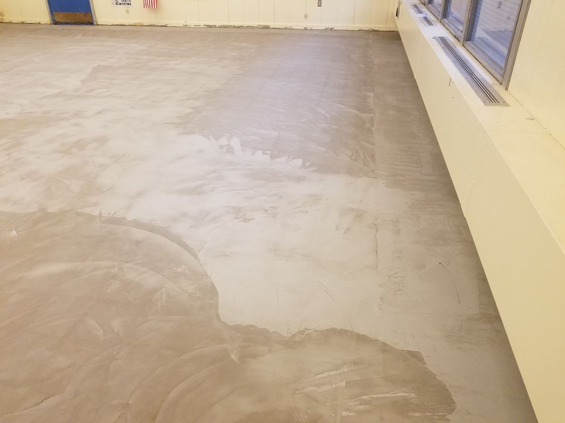 Gray concrete floor, likely recently leveled or resurfaced, inside a room with a window and a wall.