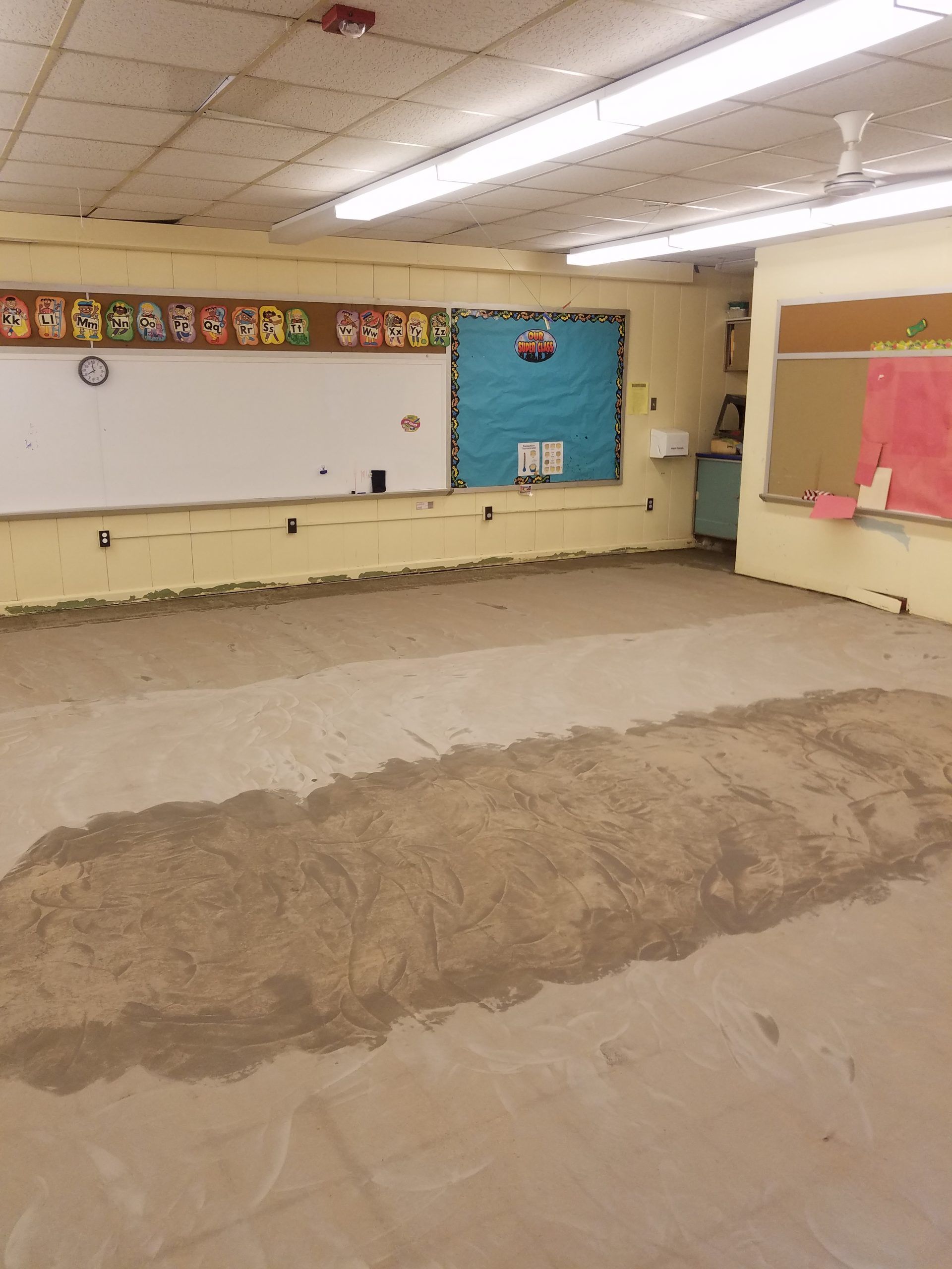 A classroom under renovation, with exposed flooring and a partially painted wall, is empty.