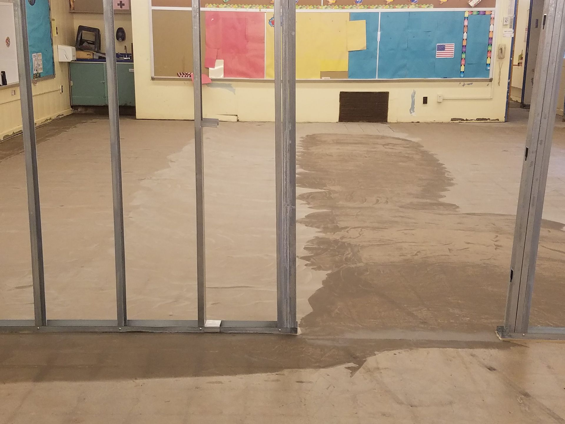 Interior view of a classroom with metal framing, newly poured concrete floor, and colorful bulletin boards.