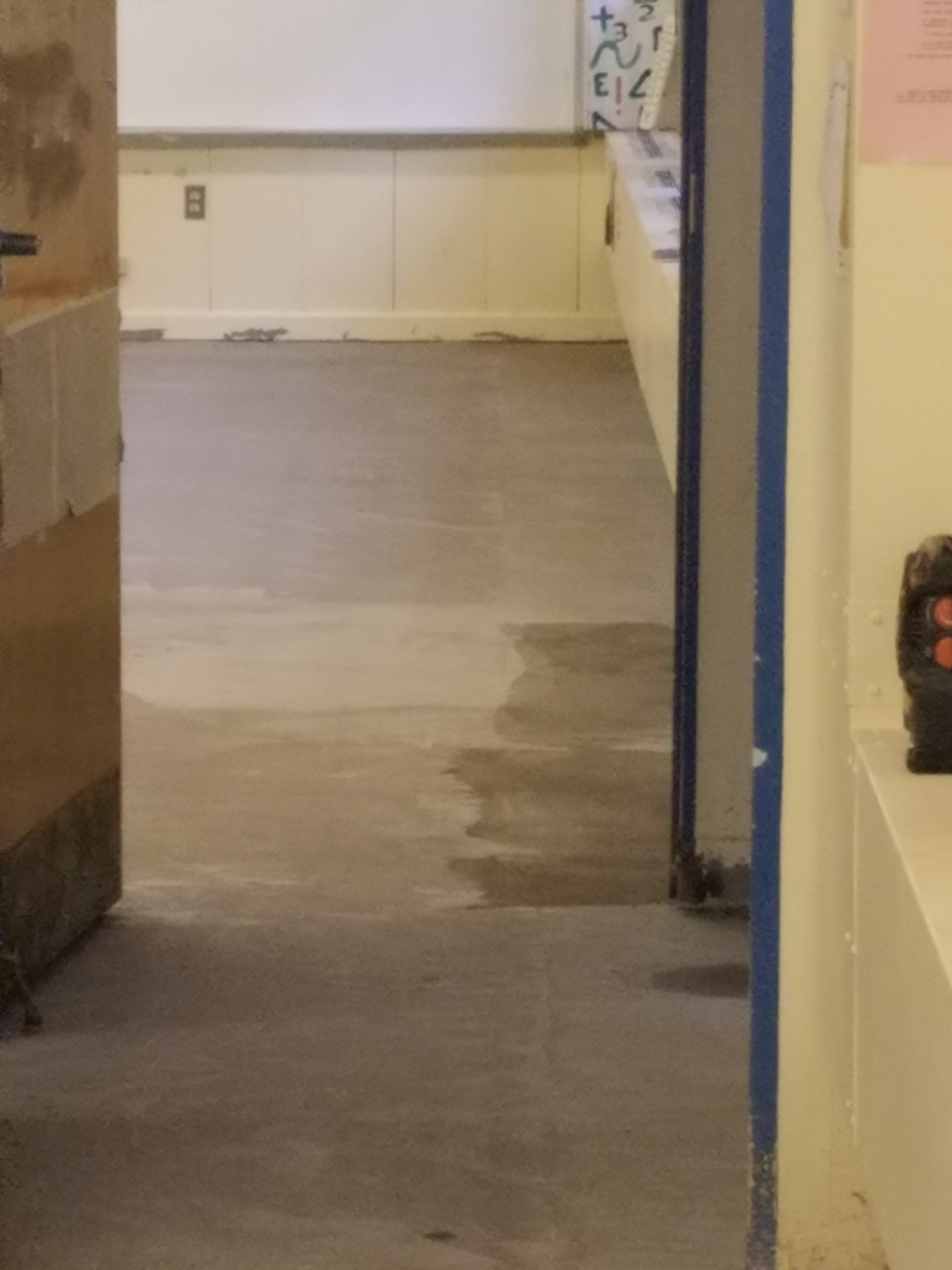 View down a hallway with cement flooring, blue doorway, and white walls.