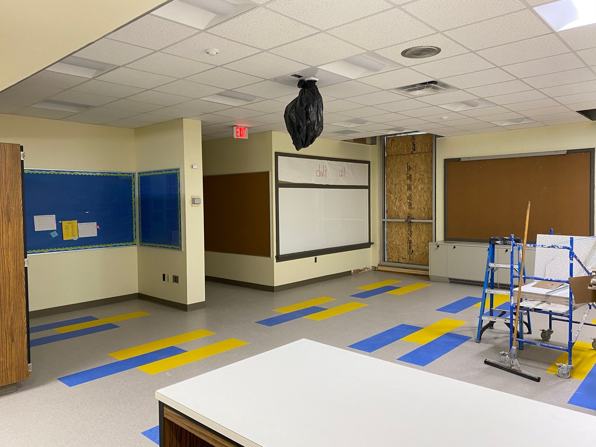 Classroom undergoing renovation with blue/yellow floor and walls, bulletin boards, and exposed ceiling.