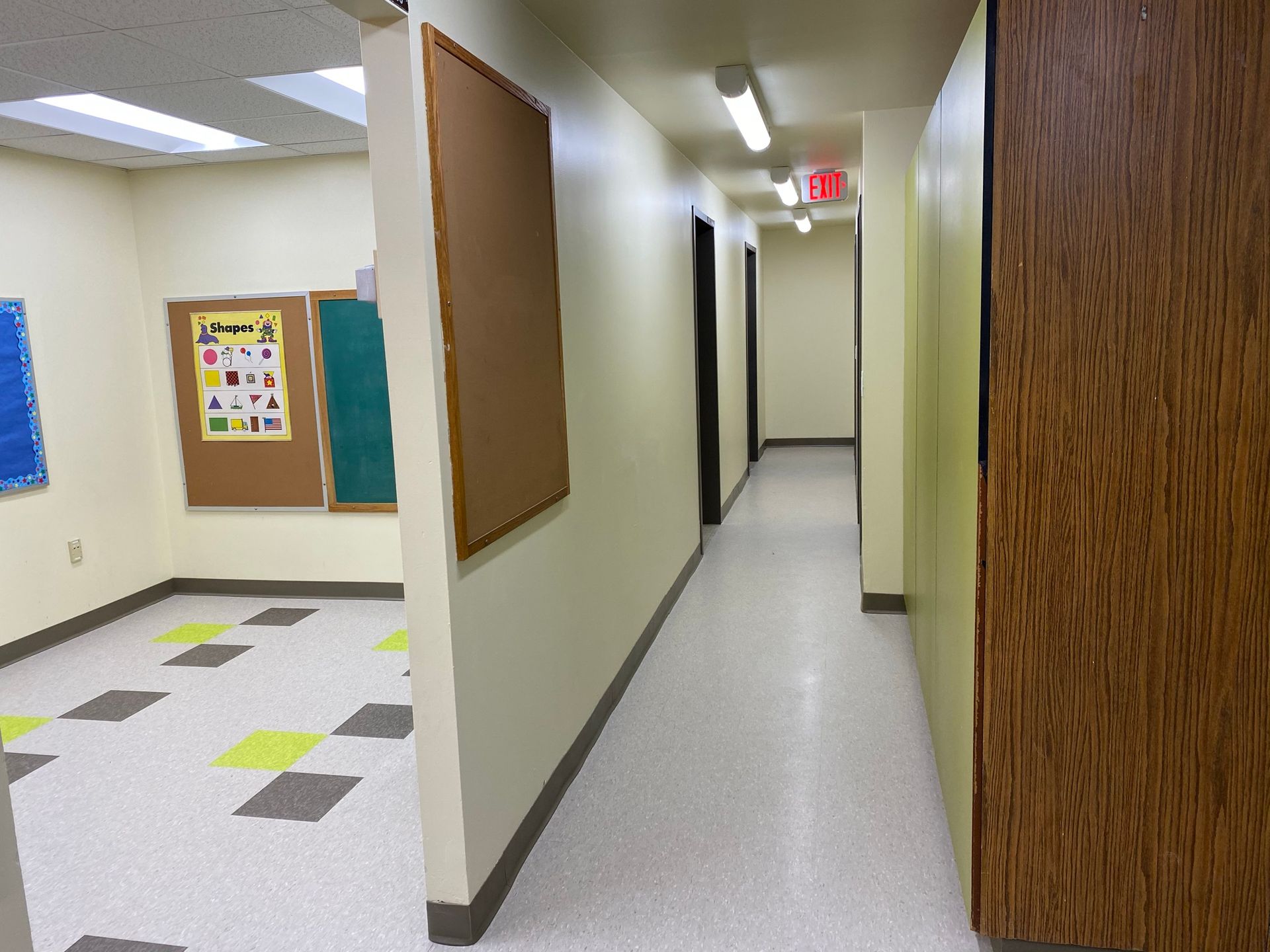 Hallway with doors, corkboard, and an open room with checkered floor and bulletin boards.