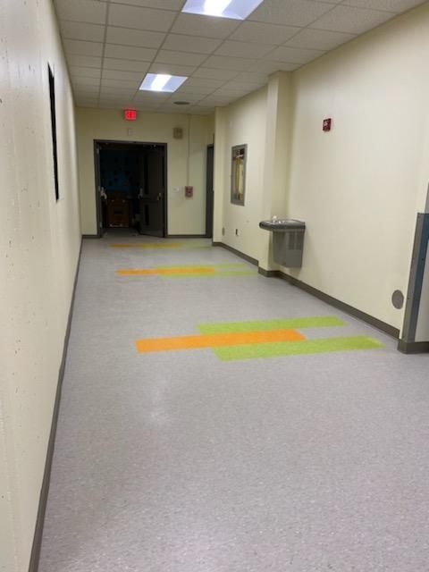 Hallway with grey floor, orange and green accents, water fountain, and exit sign.