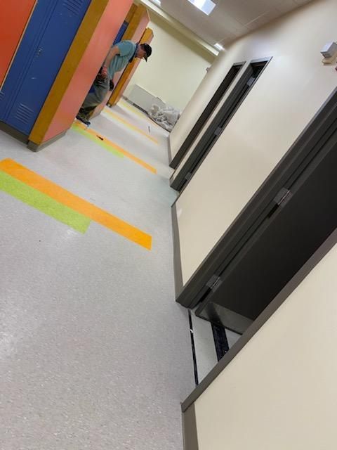 A person in a hallway with new doors and freshly painted walls.  Orange, yellow, and green markings on floor.