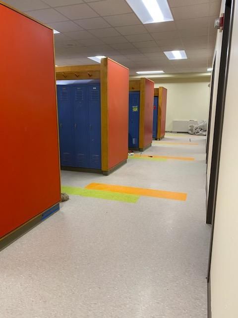 Orange and blue lockers in a school hallway with colored floor tape for social distancing.