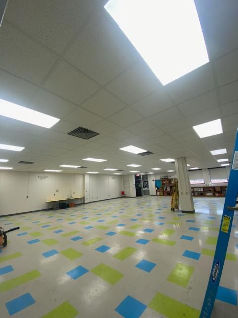 Empty room with blue, green, and white checkered floor, white walls, and bright rectangular ceiling lights. A ladder leans against the wall.