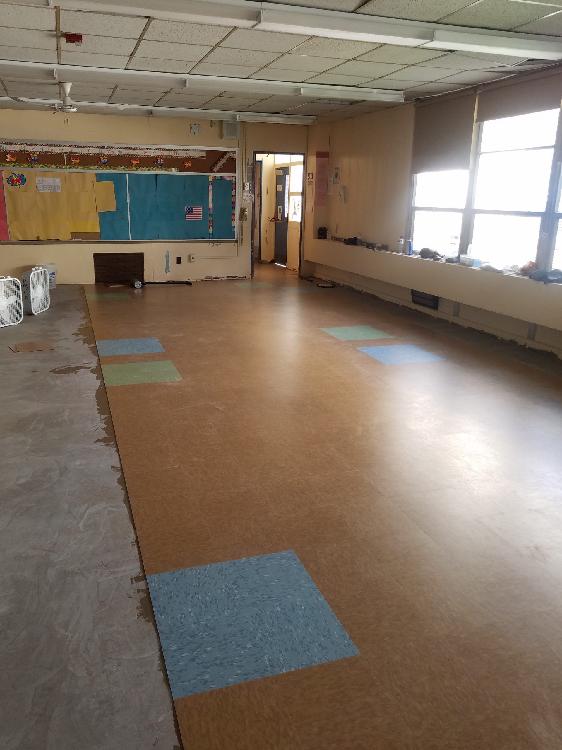 Empty classroom undergoing renovation, showing exposed ceiling, damaged walls, and partial flooring.