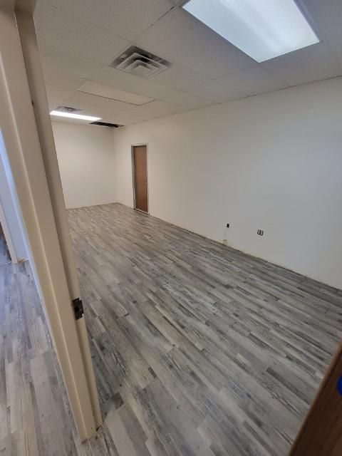 Empty room with light wood-look flooring, white walls, and a closed brown door in the background.