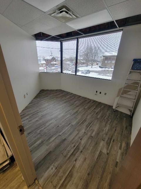 Empty room with large angled window, wood-look flooring, white walls, and a ladder.