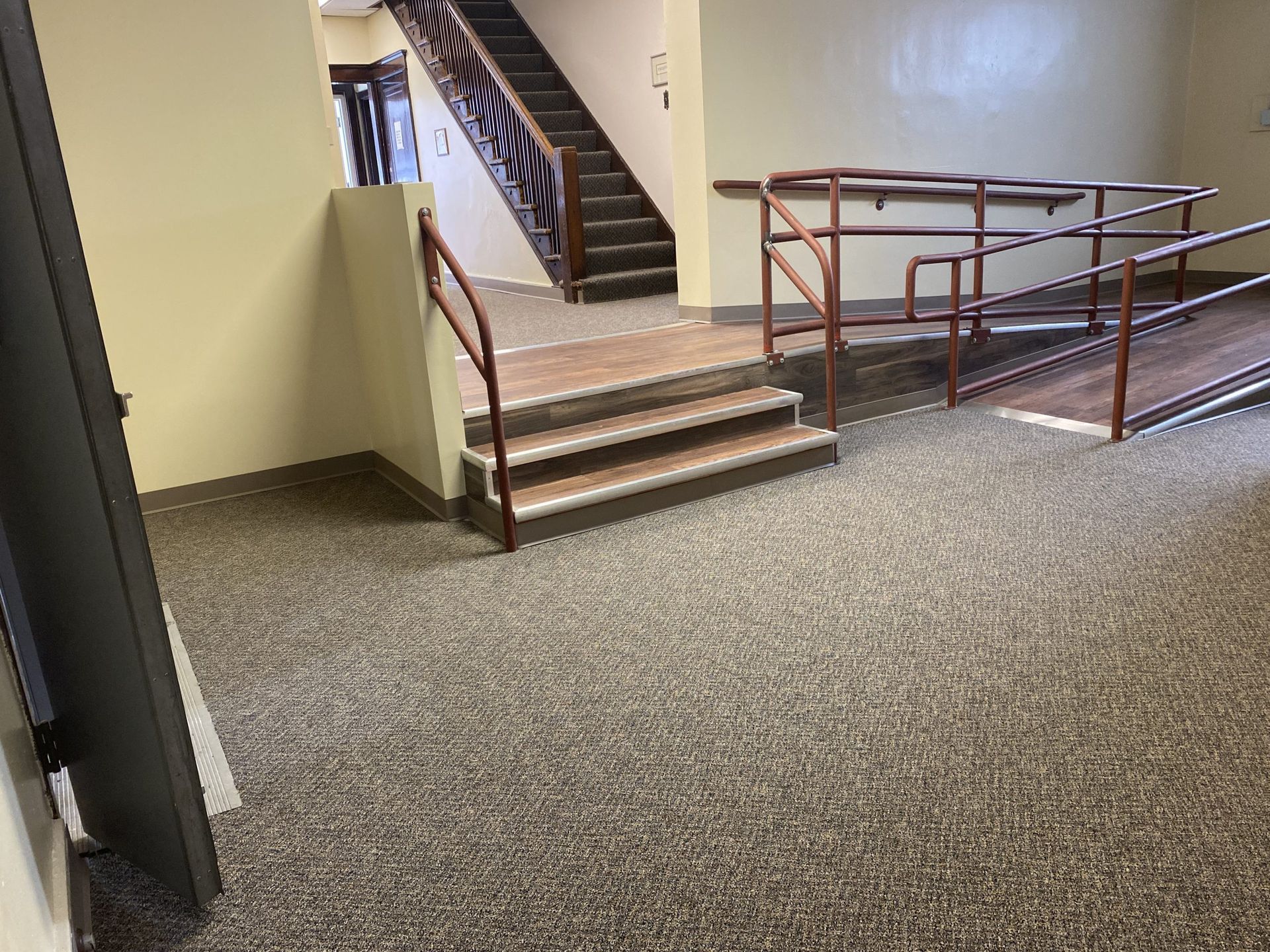 Interior with stairs, ramp, and brown handrails. Beige walls, speckled floor.