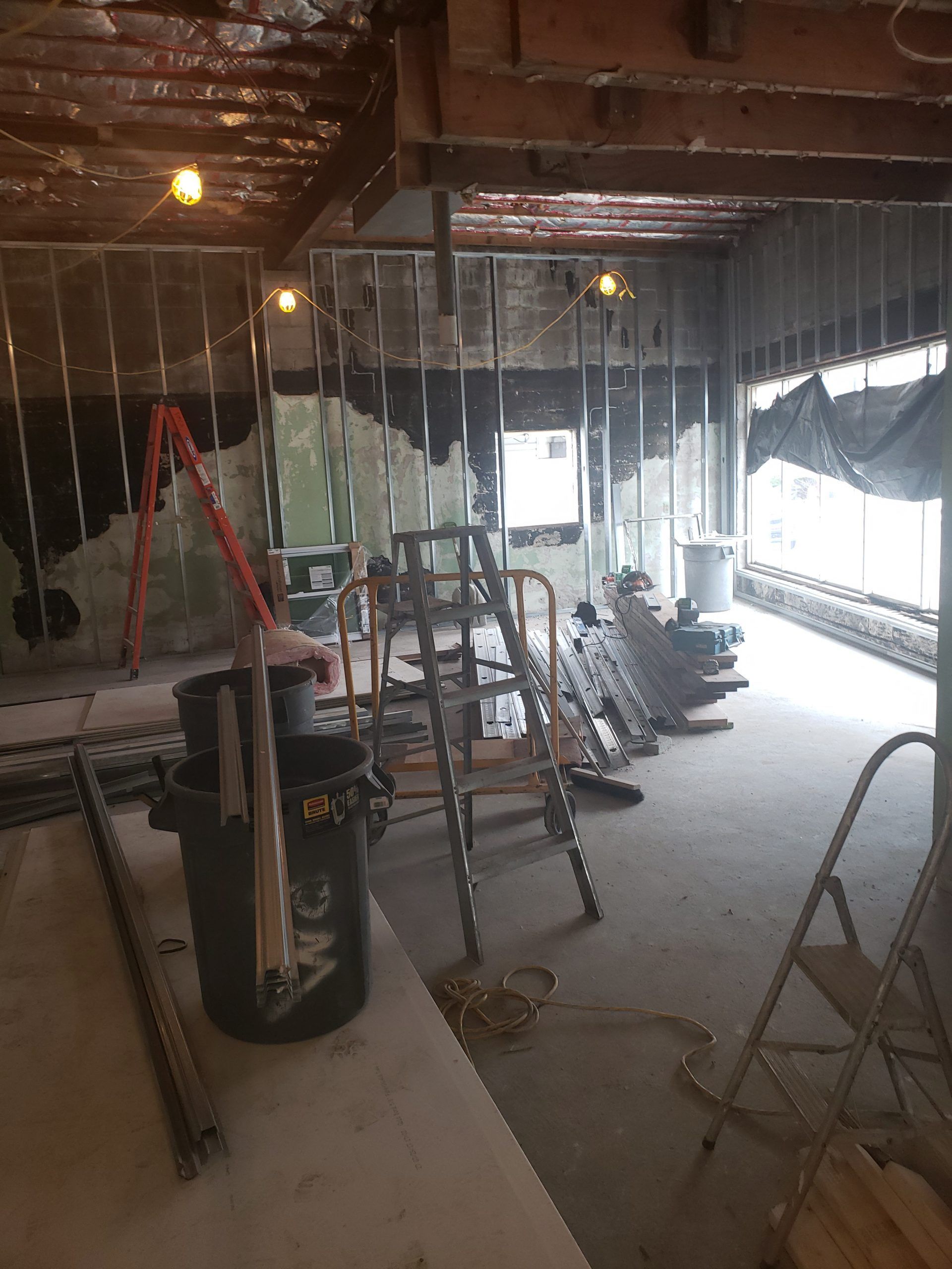 Construction site with exposed framing, debris, ladders, and buckets; interior view.